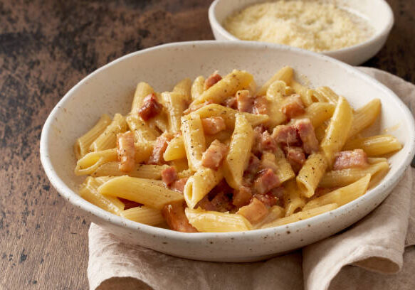 Carbonara pasta. Penne with pancetta, egg, parmesan cheese and cream sauce. Traditional italian cuisine. Side view, close up